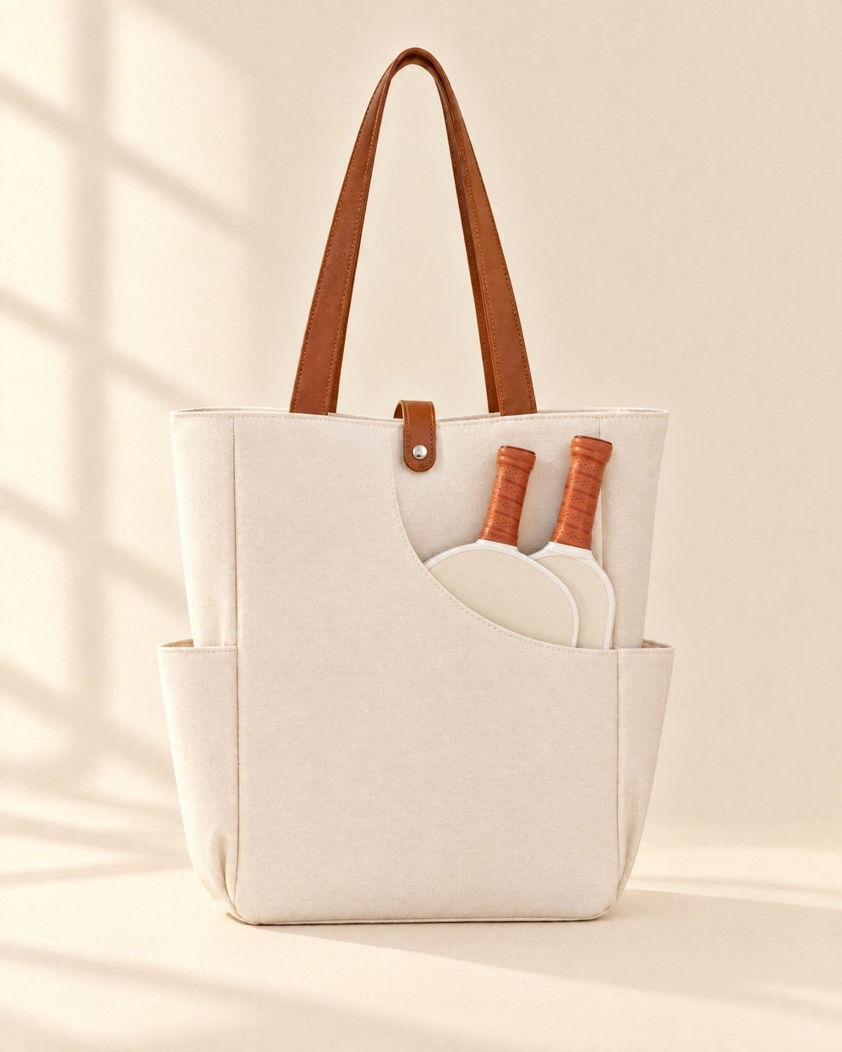 The white Caleta Tote with two pickleball paddles in the curved front pocket