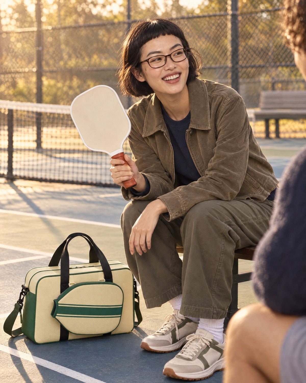 A woman at a pickleball court with the green Condesa Tote at her feet and a paddle in her hand