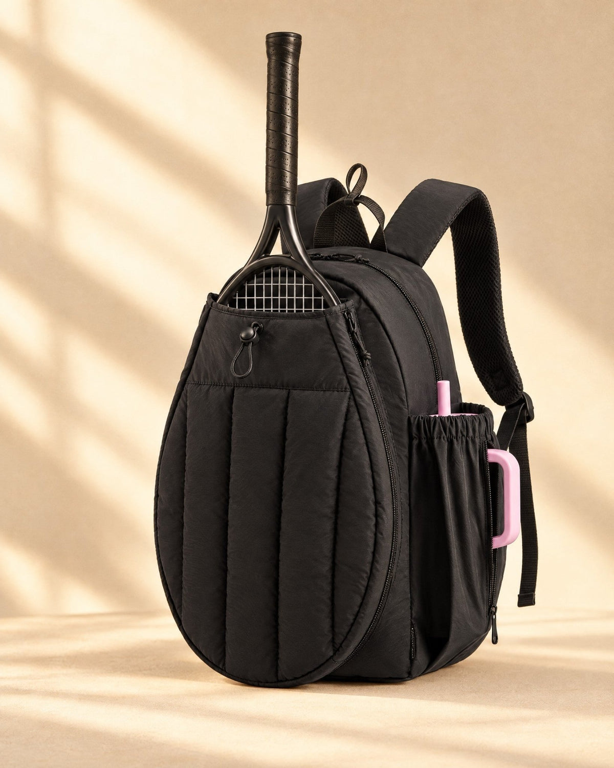 The Papagayo Backpack in black, quilted, with a tennis racket in its front pocket