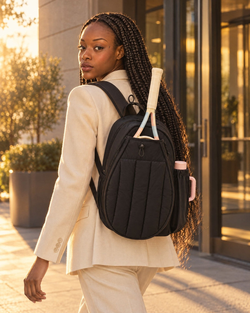 A woman in a cream blazer leaving an office with the black Papagayo Backpack and a racket in its front pocket