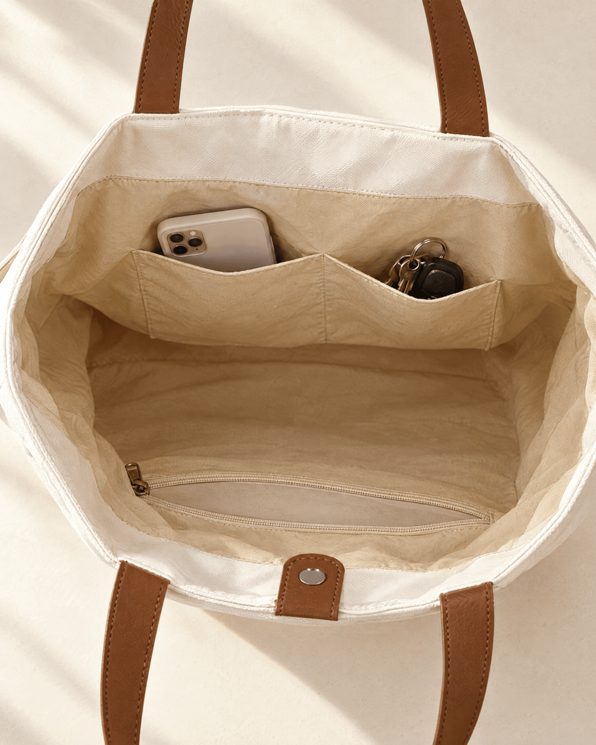 Inside the white Caleta Tote: two slip pockets holding a phone and keys, and a zipped pocket